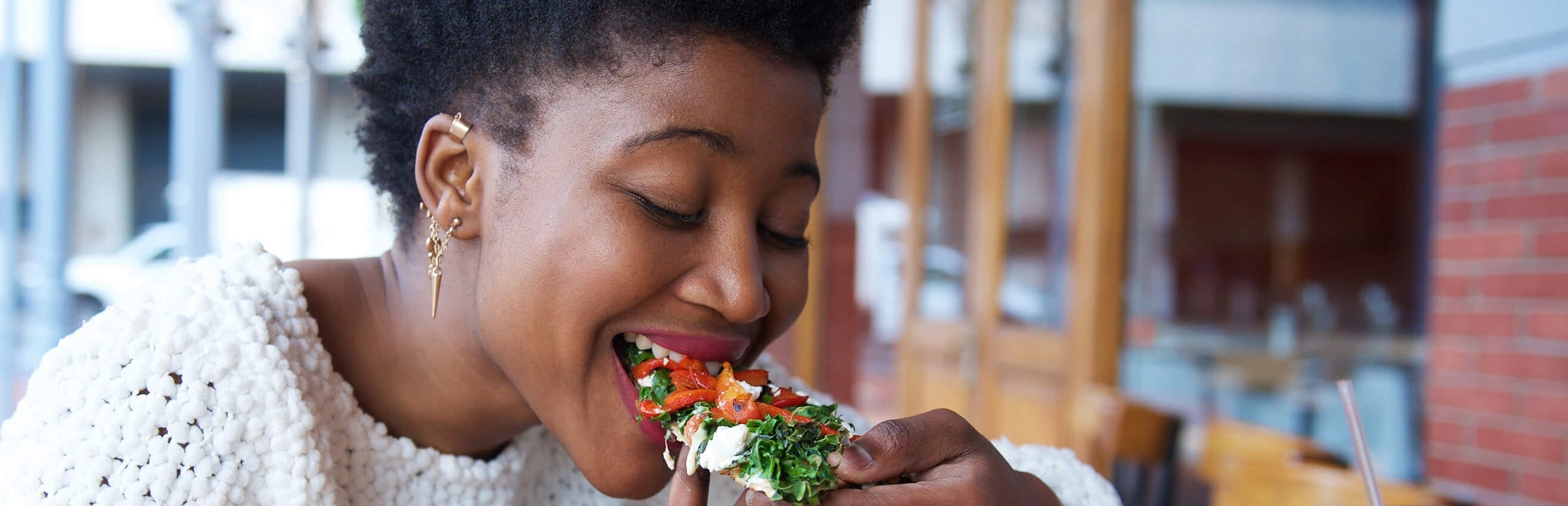 Student eating a flatbread with spinach, tomato and cheese