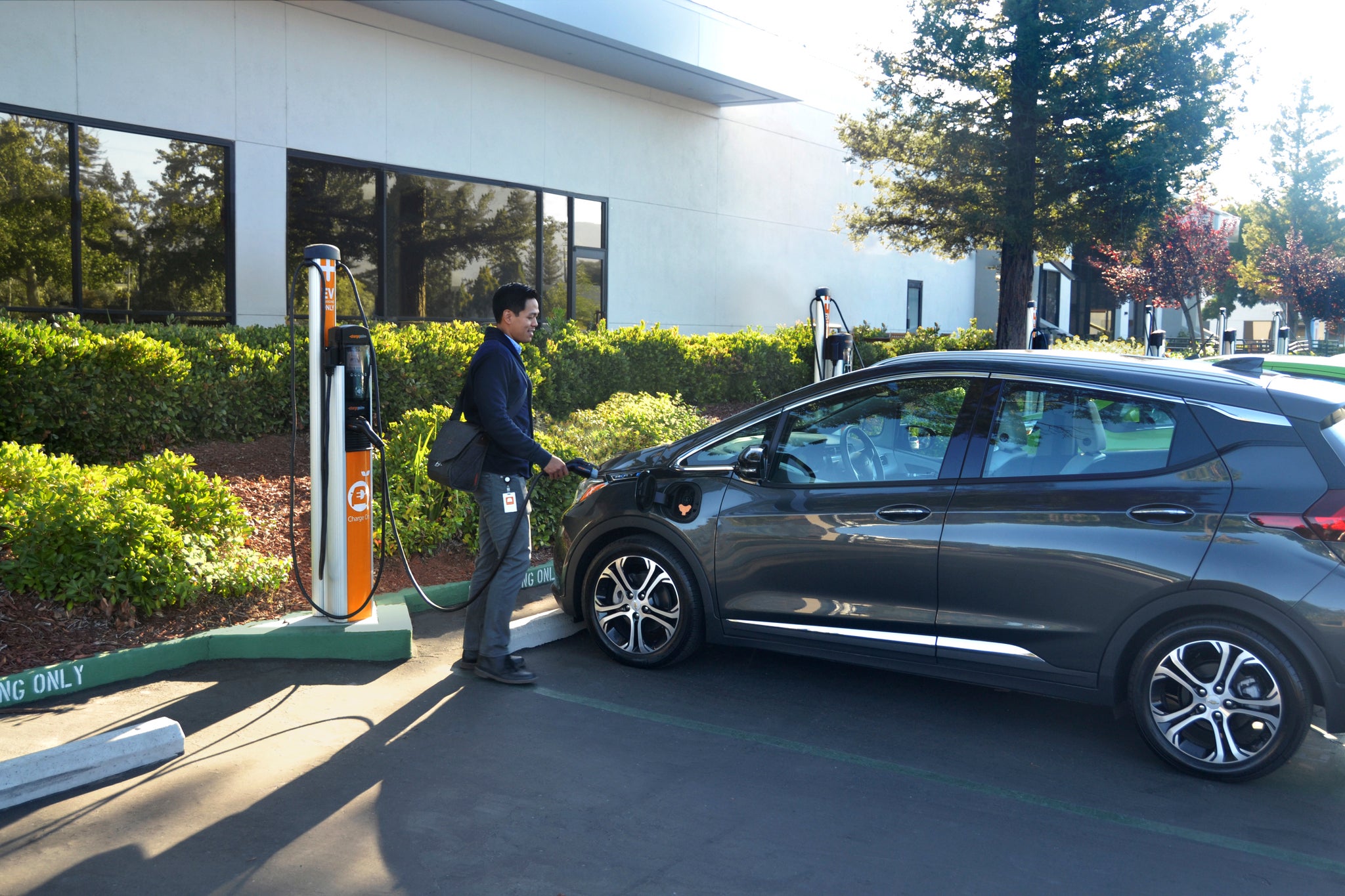 Young man charging his electric vehicle outside the office.