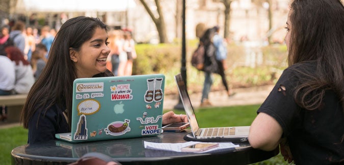 Female students sitting outside using laptops.