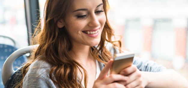 Woman sitting on bus smiling at iPhone