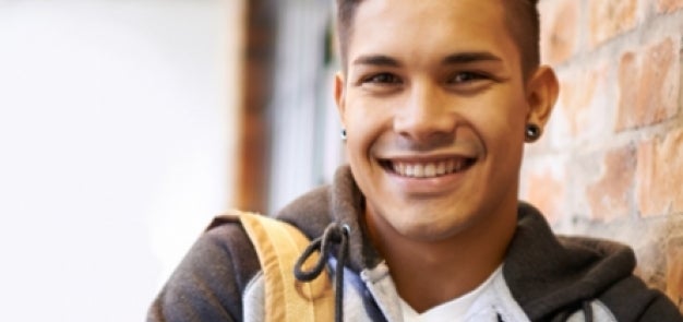 Student smiling leaning against brick wall