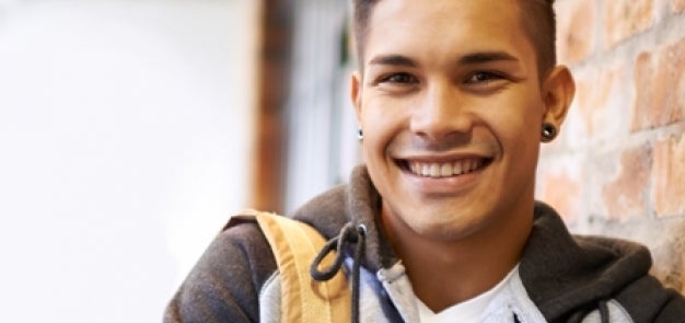 Student smiling leaning against brick wall